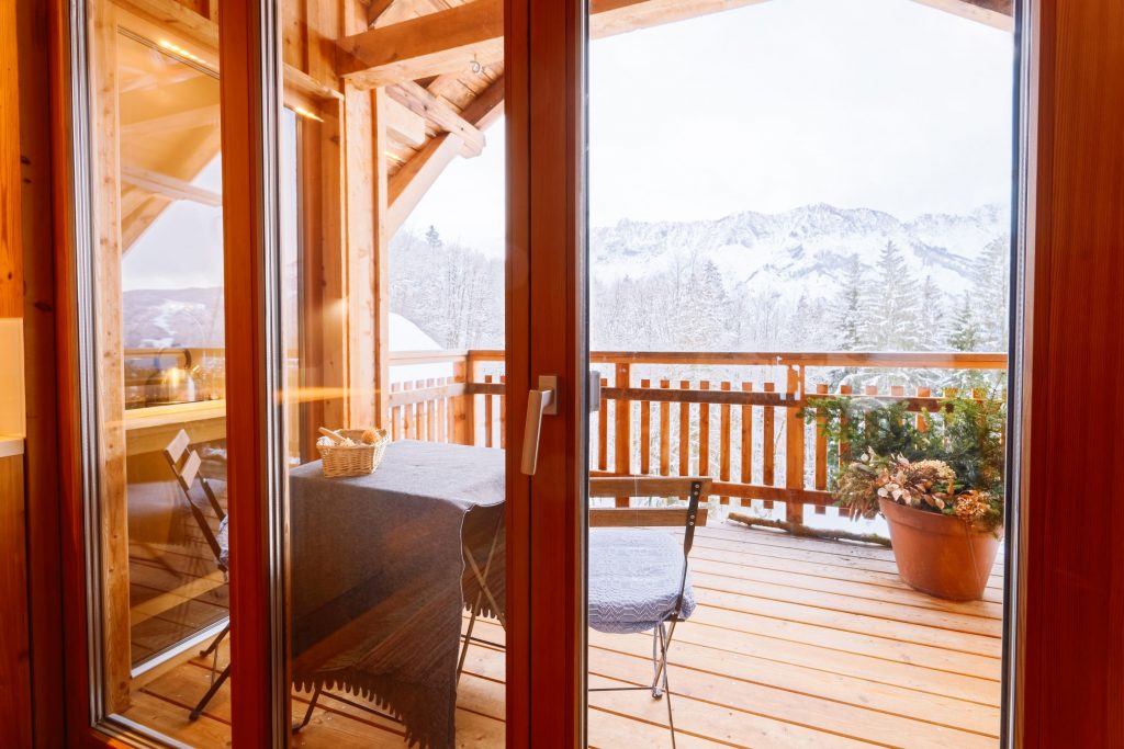 View from Balcony of living room on Austrian Alps mountain in snow winter. Design of modern apartment house with open terrace and Alpine scenery in Austria. Decor. Stylish lifestyle. Table with chairs