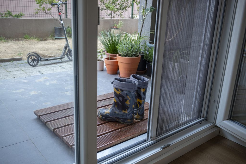 Dirty boots in front of a patio door and there is a sliding mosquito wire at the door.
